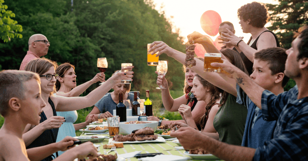 summer gathering of people outside eating dinner at a table and toasting with their drinks
