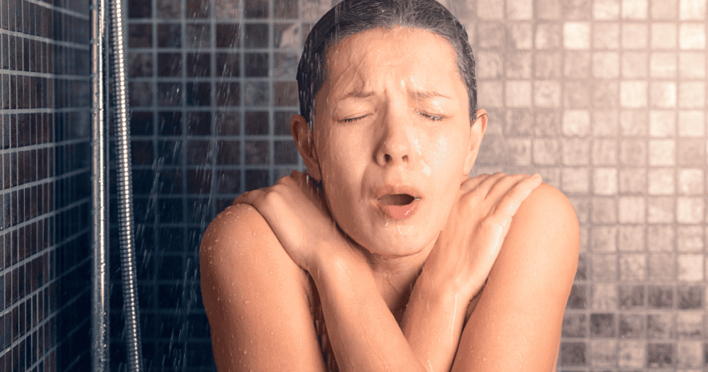 woman reacting to a cold shower by grabbing her shoulders